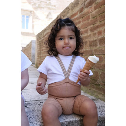 Ein kind trägt kurze strumpfhose mit träger in hellbraun gestreift und beige gestrickte overalls hält eine vanilleeistüte
