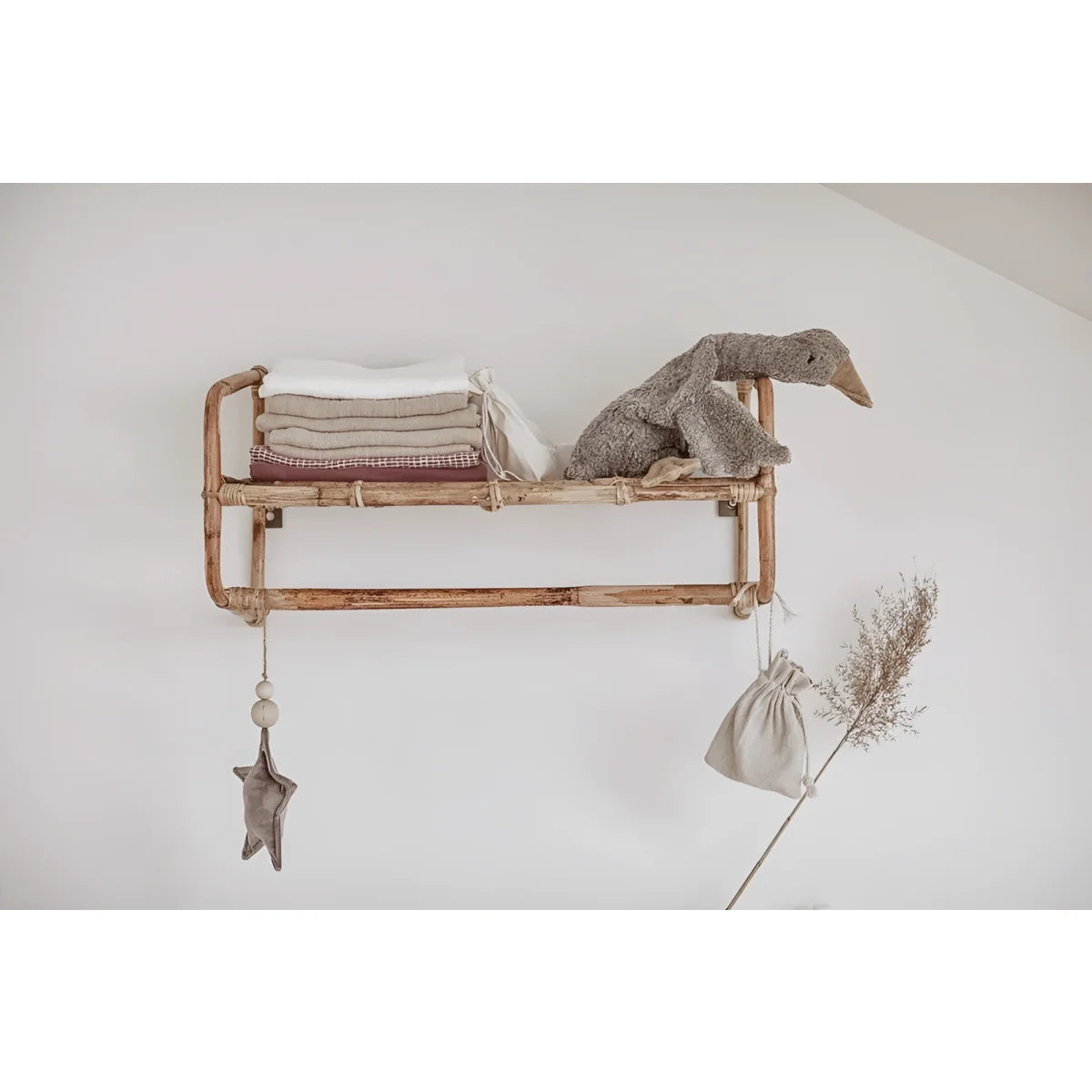 Holzregal mit Kupferrohren, gefalteten Textilien und Kuscheltier Gans klein in grau