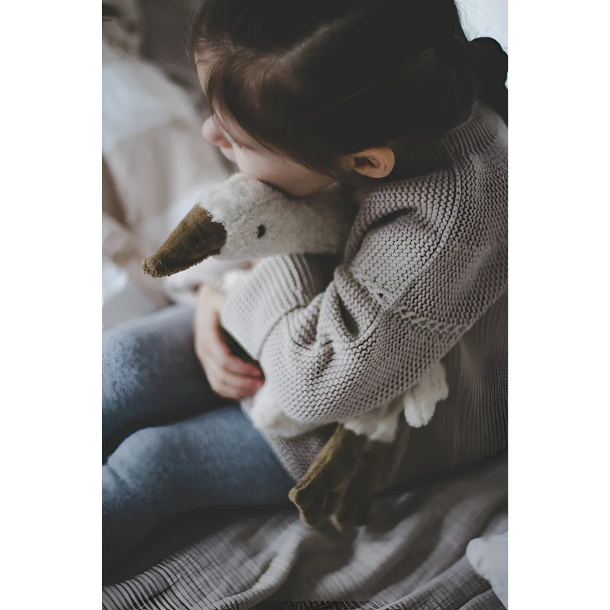 Kind umarmt ein kleines weißes Kuscheltier Gans