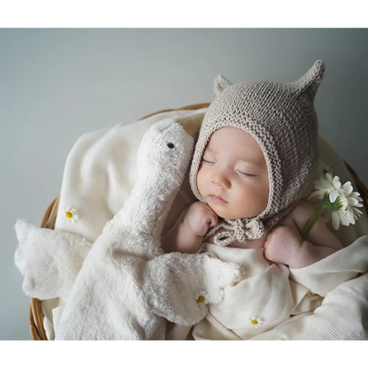 Schlafendes Baby mit gestrickter Mütze und Kuscheltier Gans klein in Weiß