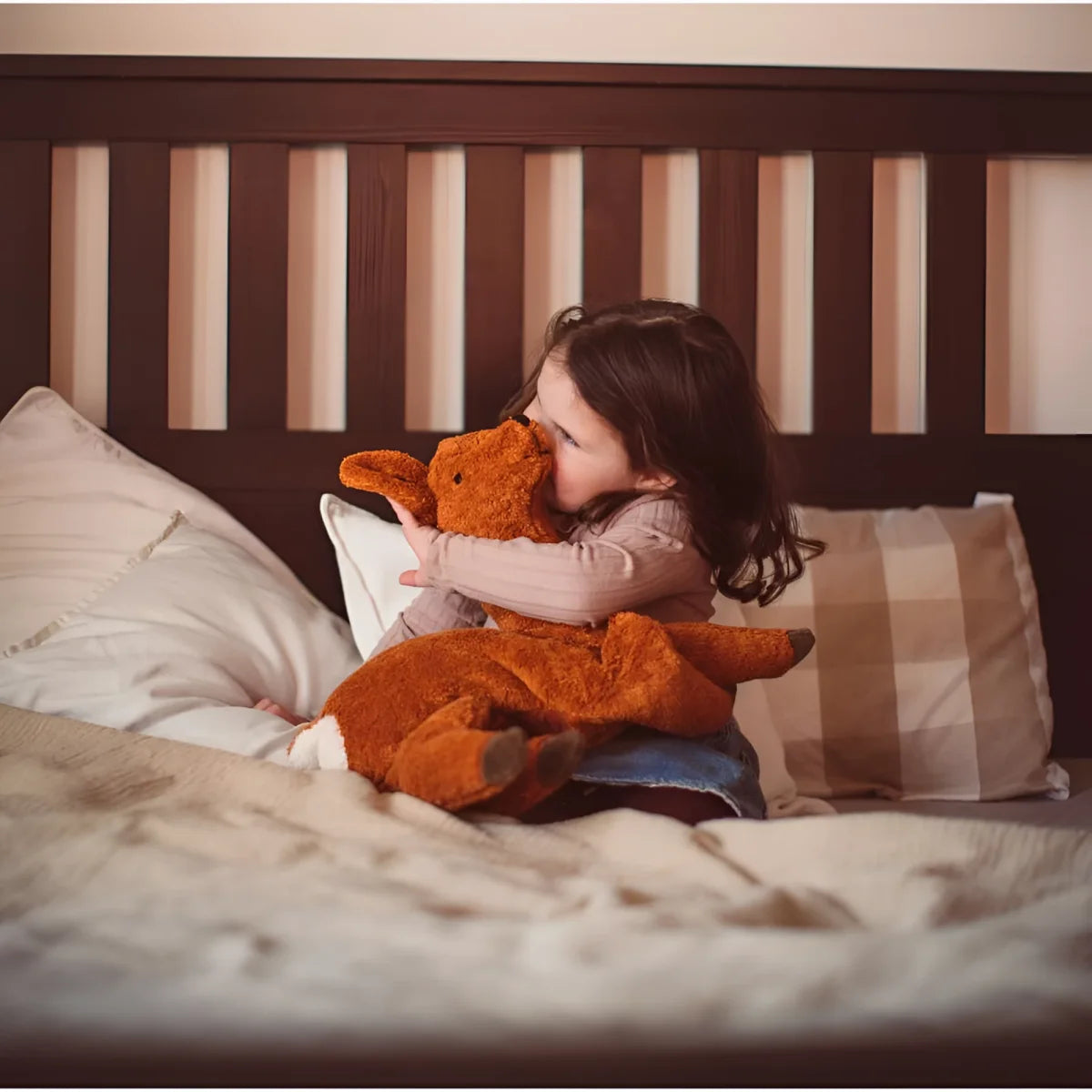 Kind umarmt orangefarbiges Plüschdinosaurier auf Bett neben Kuscheltier Reh groß