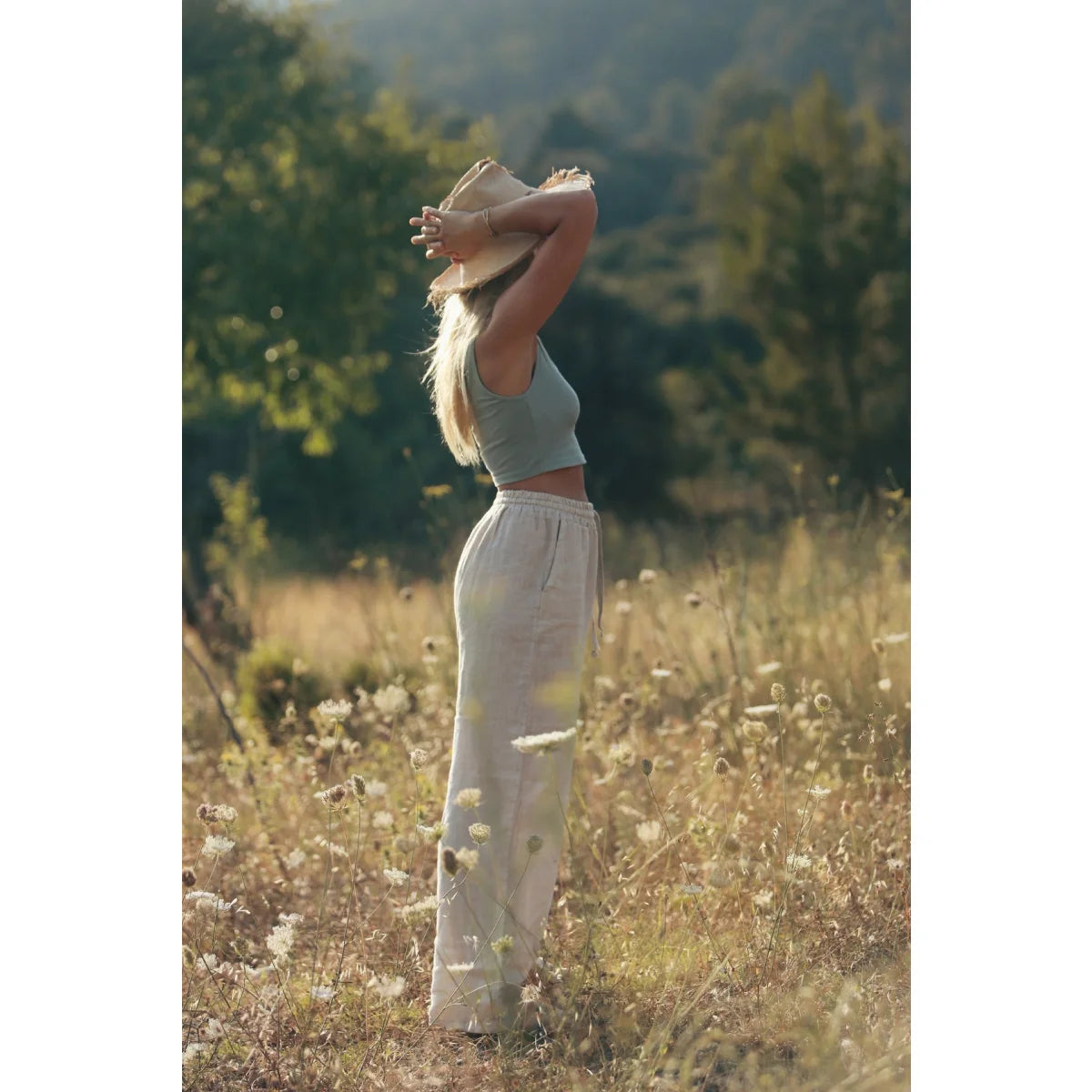 Frau in weißen Hosen und Crop-Top dehnt sich auf sonnigem Feld mit Leinen Hose Isla