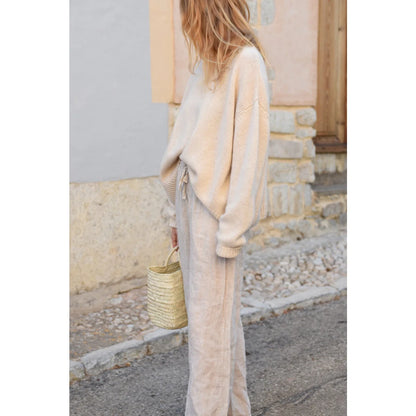 Frau in beiger Oversized-Strickjacke und heller Hose mit einem geflochtenen Korb