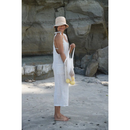 Frau im weißen Sommerkleid und Sonnenhut mit einer Netztragetasche im Leinen Overall