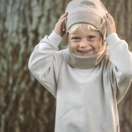 Lächelndes Kind in creamfarbenem Outfit und Hut, trägt Lounge Sweater Rib Strick beige
