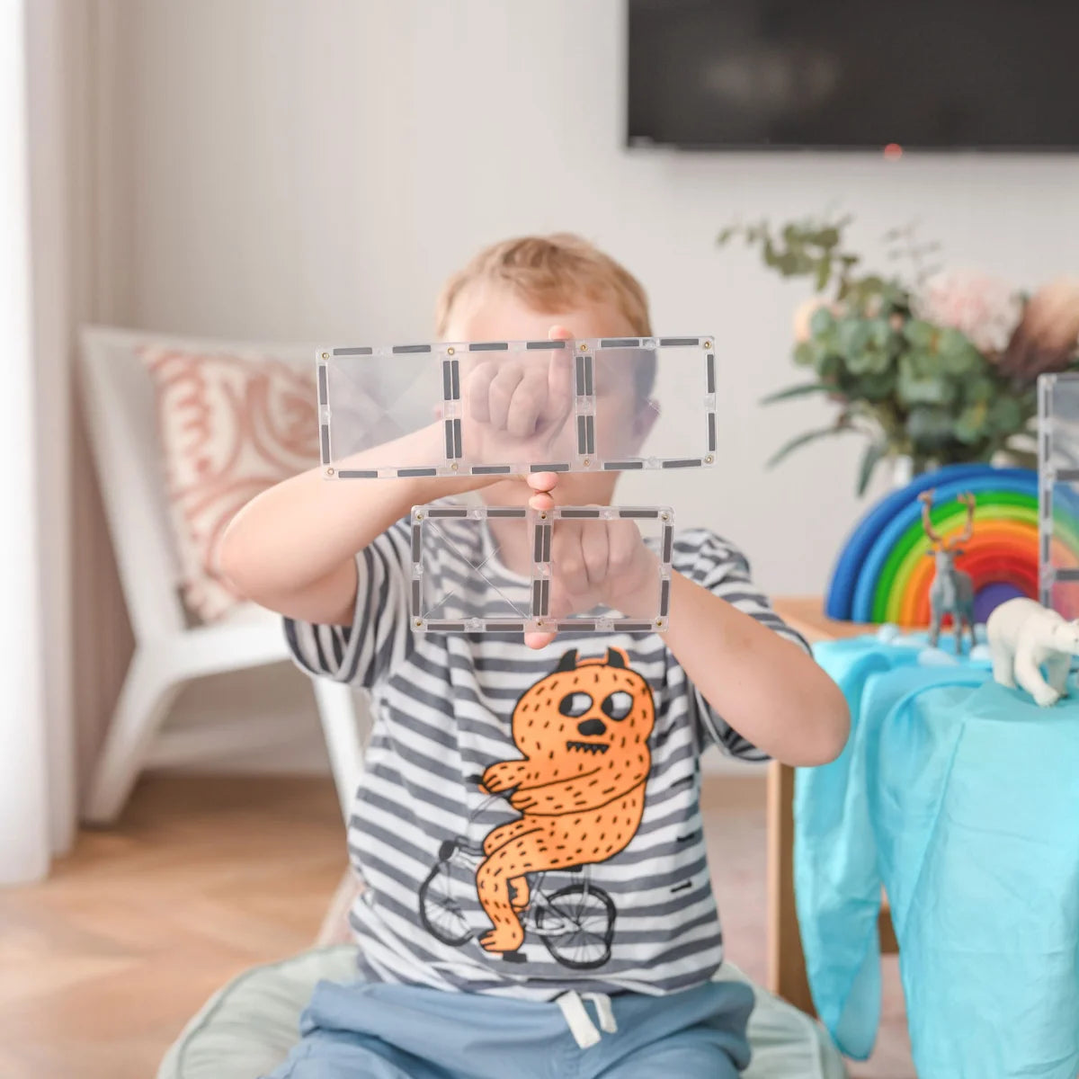 Kind trägt gestreiften T-Shirt mit orangefarbener Monstergrafik für Magnetbausteine