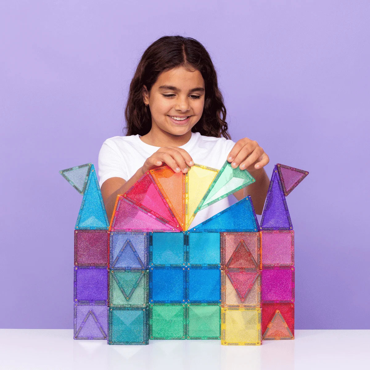 Lächelndes Mädchen spielt mit bunten, durchsichtigen Magnetbausteinen aus dem Glitter Castle Pack