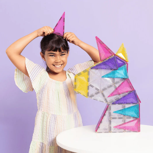 Junge Frau mit gestreiftem Kleid hält pinken Magnetstein neben buntem Magnet- Einhorn