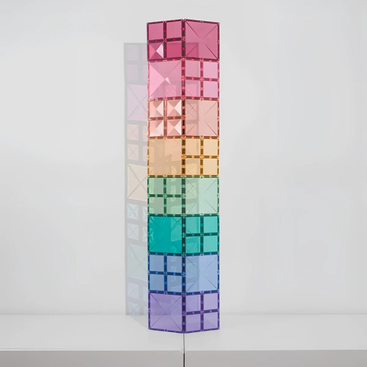 Ein hoher turm aus 40 pastellfarbenen magnetbausteinen in regenbogenfarben von rosa bis lila aus durchsichtigem material
