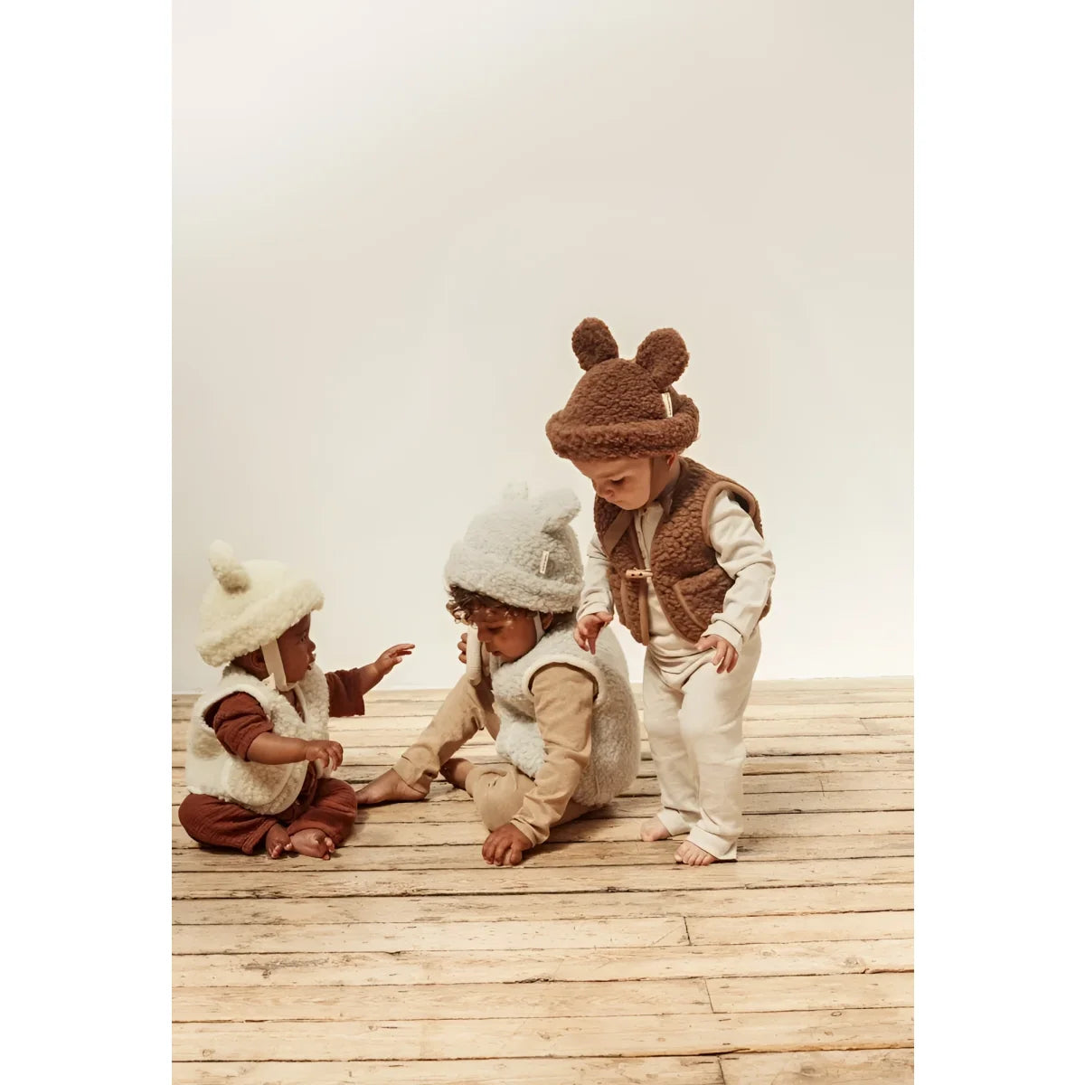 Drei Babys in Wollmützen und -westen mit dem Merino Hat von Bruno