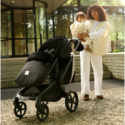 Schwarzer kinderwagen mit plüschfell gefüttertem sitzbezug und weißem bini bamba gurt nachhaltige babykleidung schweiz