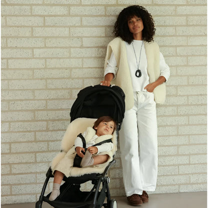 Schwarzer kinderwagen mit cremefarbenem merino mama gilet aus nachhaltiger babykleidung schweiz und sheepskin liner