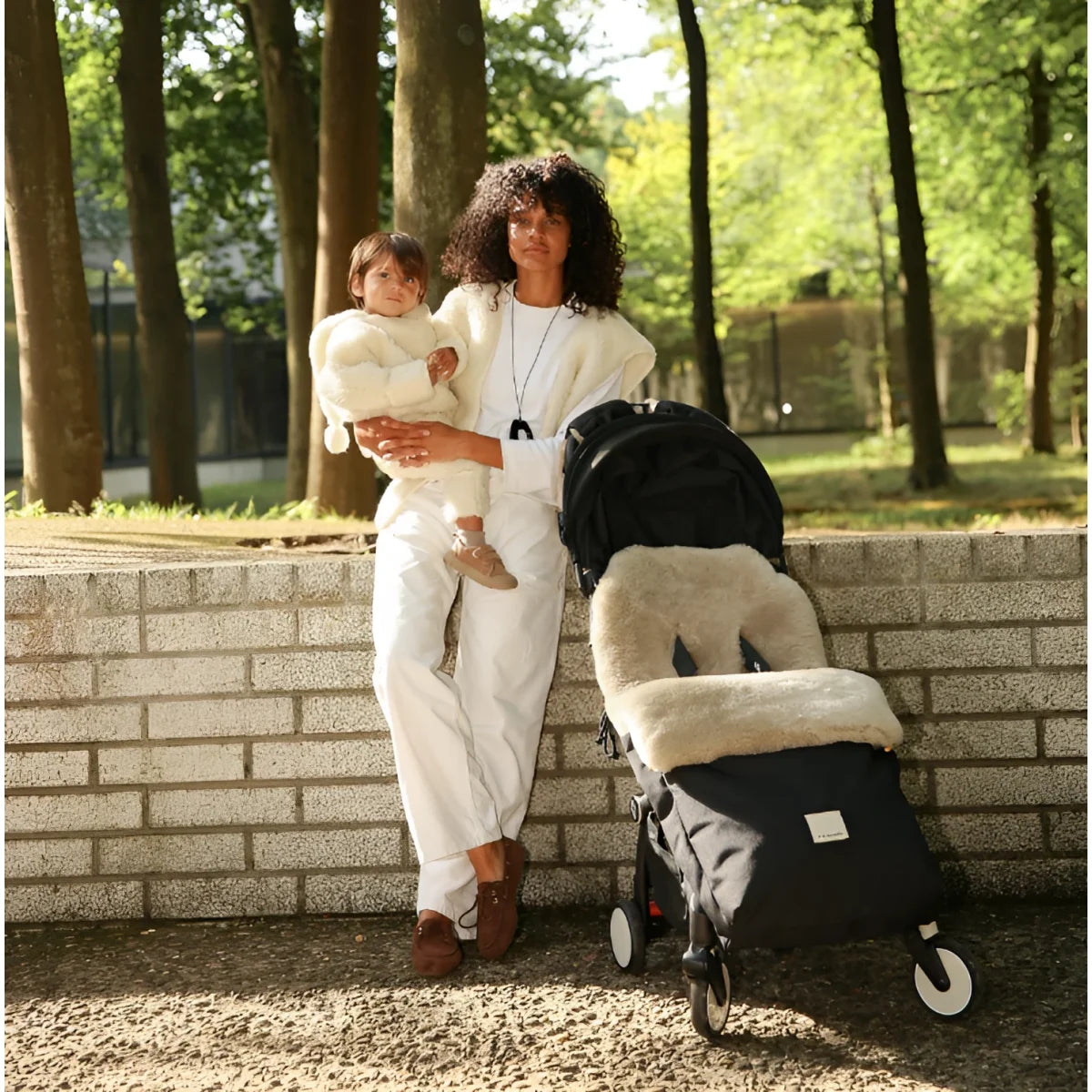 Schwarzer kinderwagen mit beigem merino mama gilet sheepskin sitz- und fussmuff für nachhaltige babykleidung schweiz