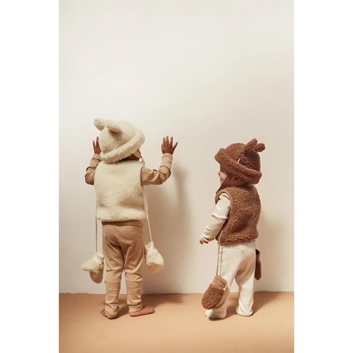Zwei Kinder in flauschigen Tier-Overall-Kostümen stehen vor einer Wand