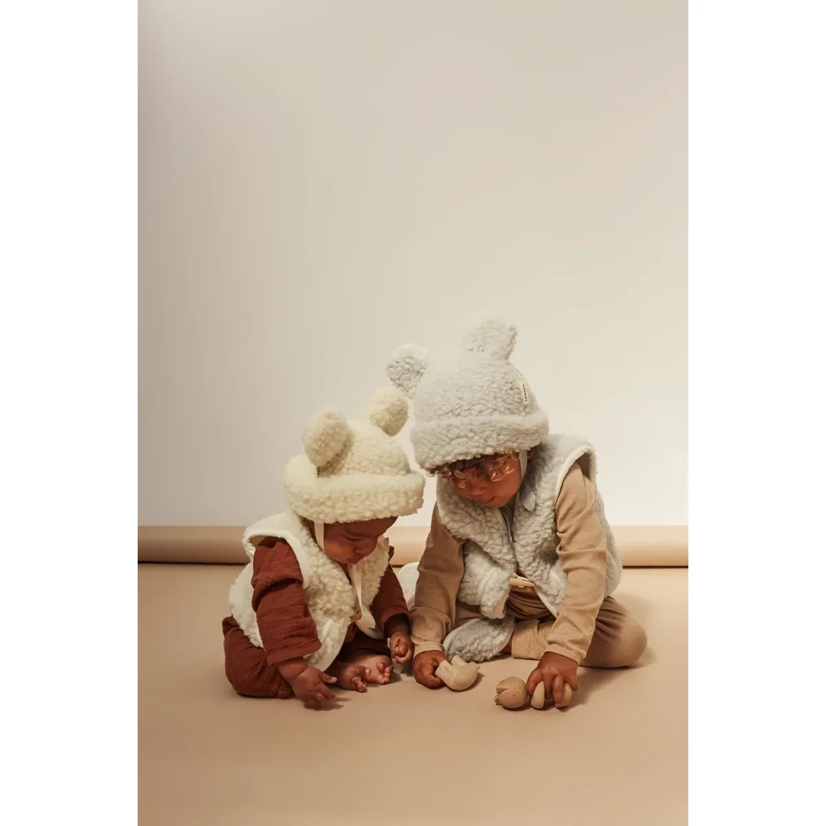 Zwei Kinder in warmen Winterhüten und Jacken sitzend auf dem Boden mit Merino Hat Milk