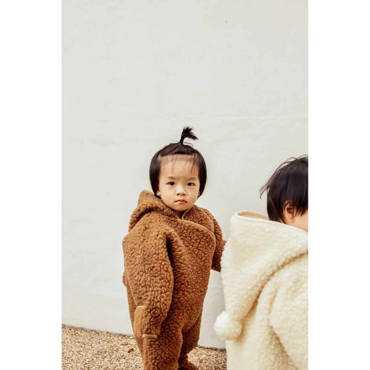 Kind im flauschigen braunen Bärenkostüm des Merino Snugglesuits Bruno