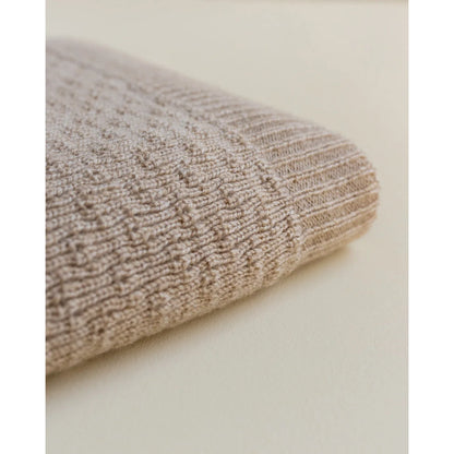 Gefalteter beiger Stoff mit Rippmuster der Merino Strickdecke Dora in Sandfarbe