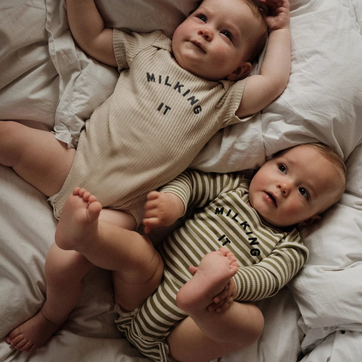 Zwei babys tragen passende milking it kurzarm-bodysuits in ockerfarbenem rippenstrick und olivgrün-gestreiftem stoff