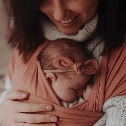 Neugeborenes Baby in pinkem Tuch, nah am Brustkorb eines Erwachsenen, Mini Bow