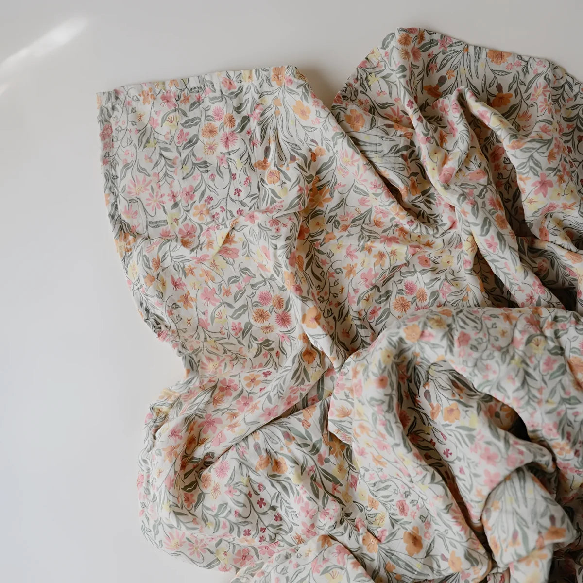 Ein mulltuch aus weichem, cremefarbenem stoff mit zartem blumenmuster in rosa und pfirsichtönen