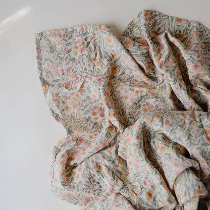 Ein mulltuch aus weichem, cremefarbenem stoff mit zartem blumenmuster in rosa und pfirsichtönen