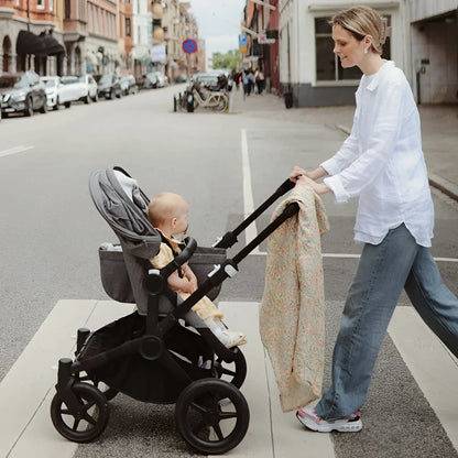 Grauer und schwarzer kinderwagen mit baby und mulltuch in pastel blooms muster