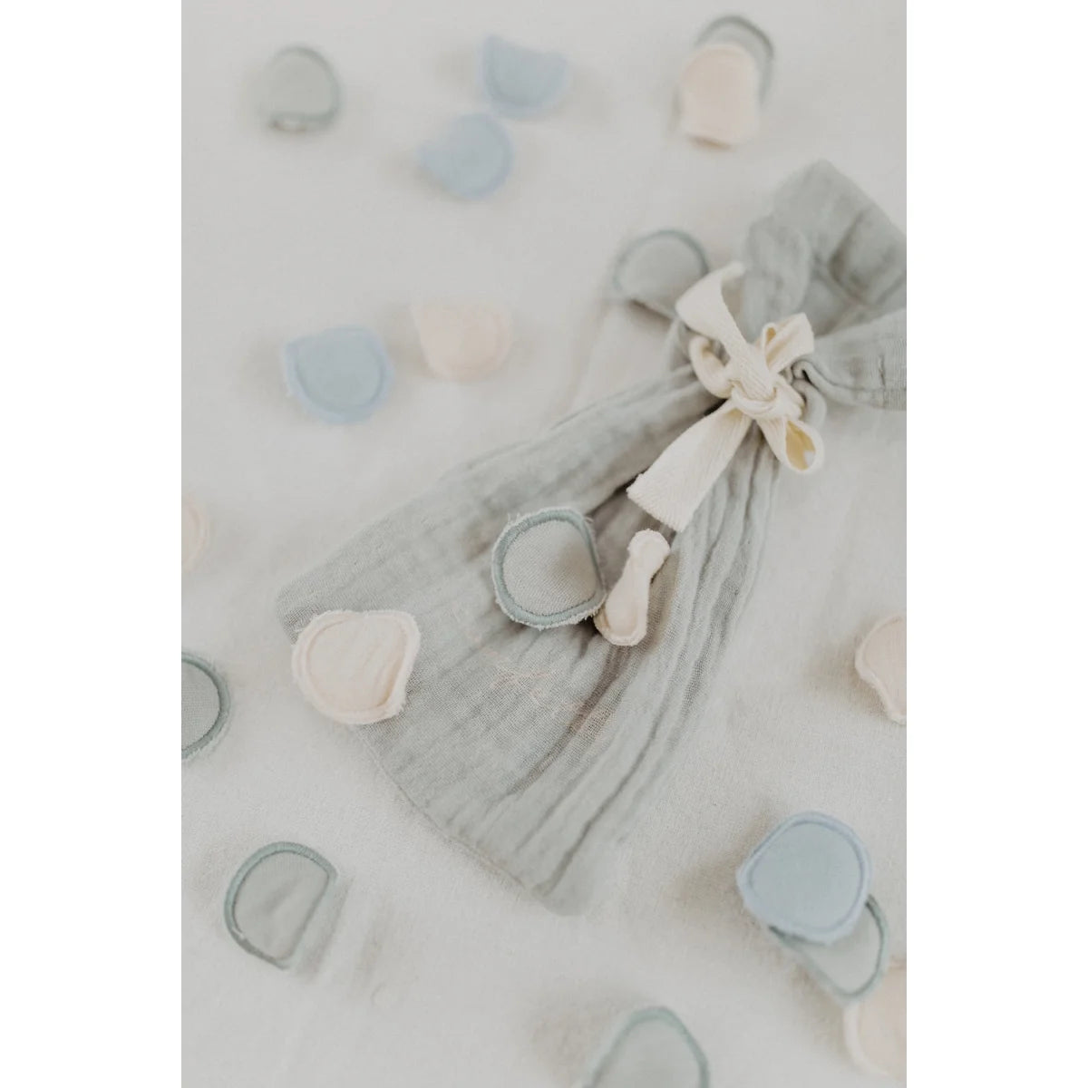 Ein weicher grauer gauze ziehbeutel mit cremefarbenem band und stoffknöpfen für nachhaltige babykleidung schweiz