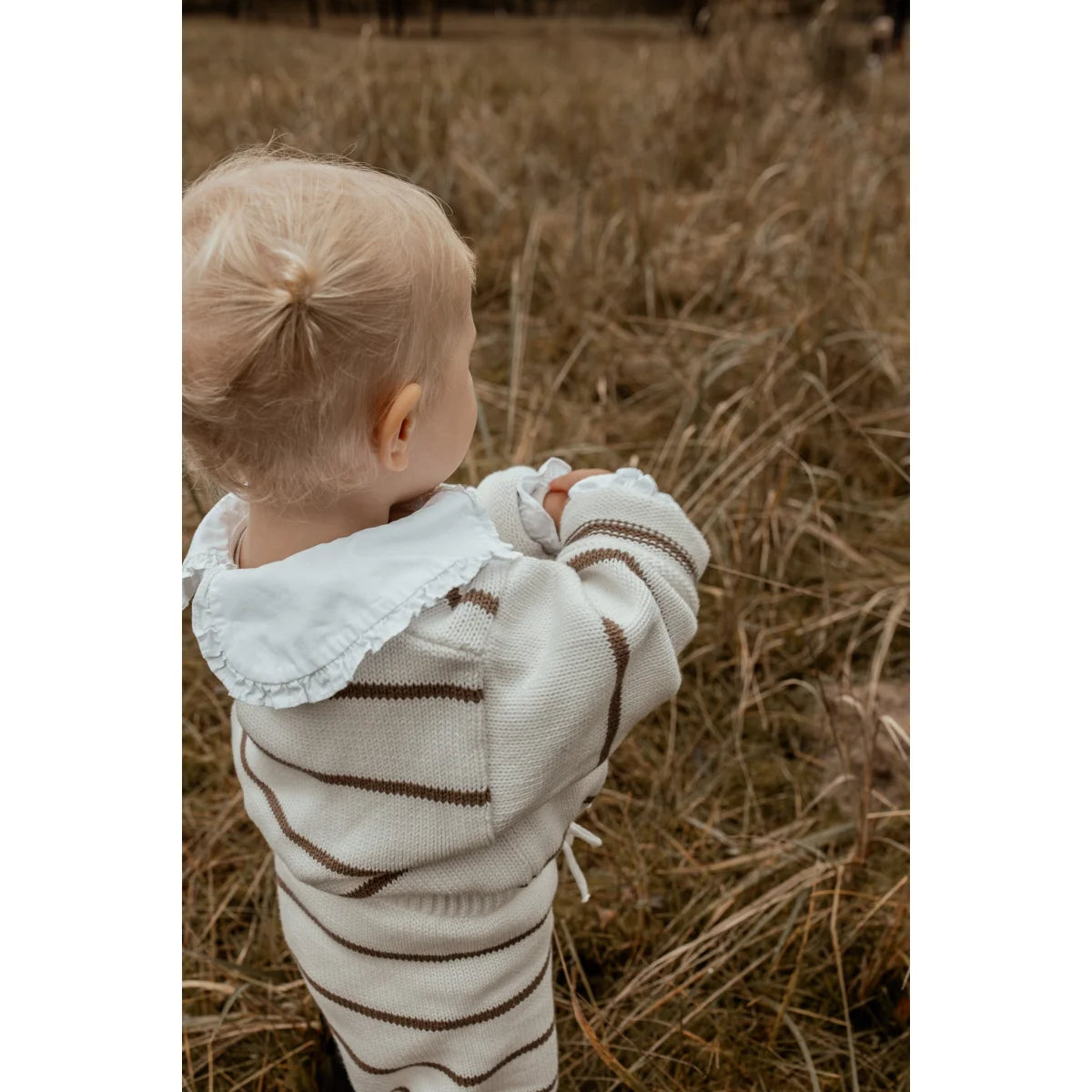 Blondes Kleinkind mit gestreiftem Pullover steht in einem Feld