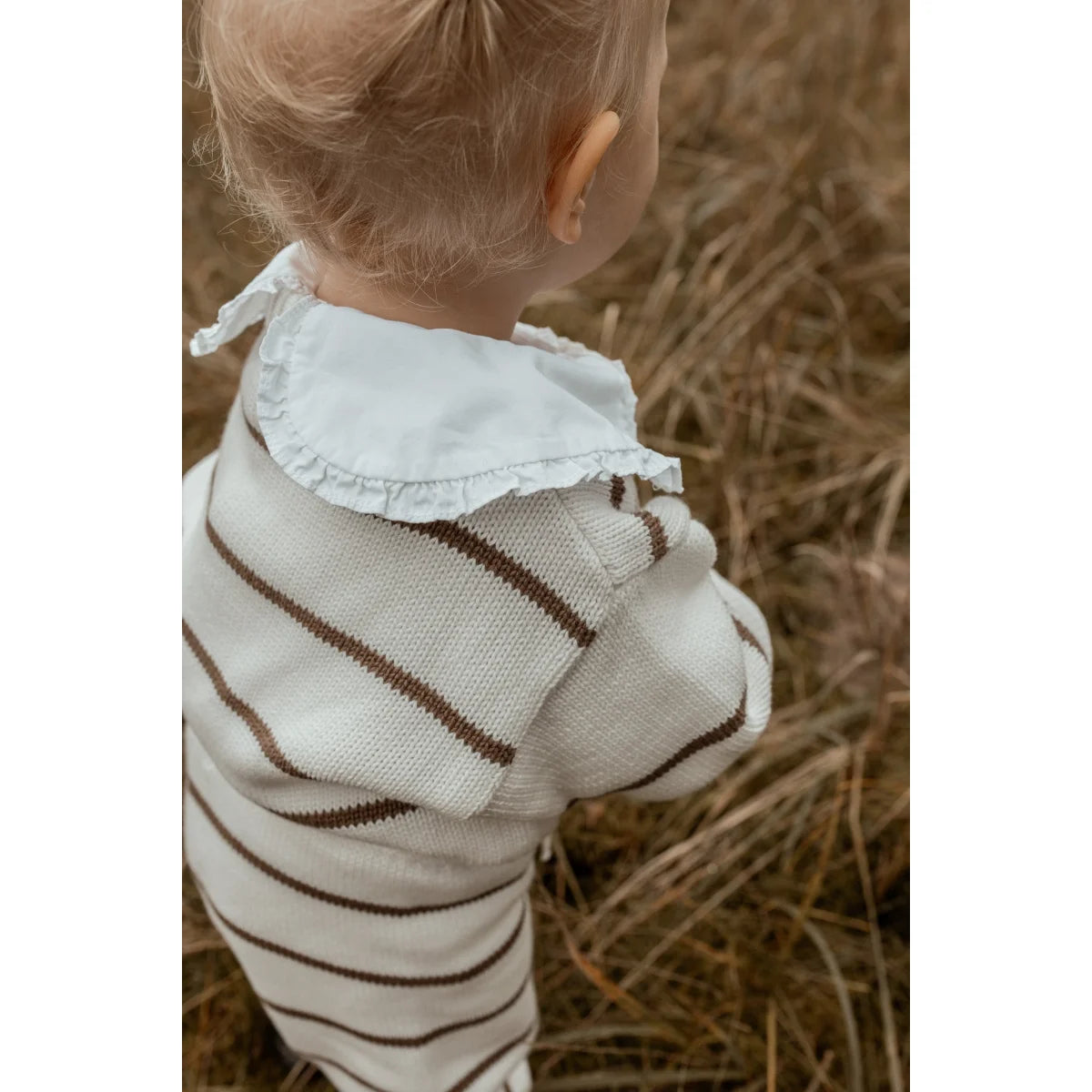 Kind trägt einen übergroßen, gestreiften Pullover in Weiß und Braun mit Rüsche