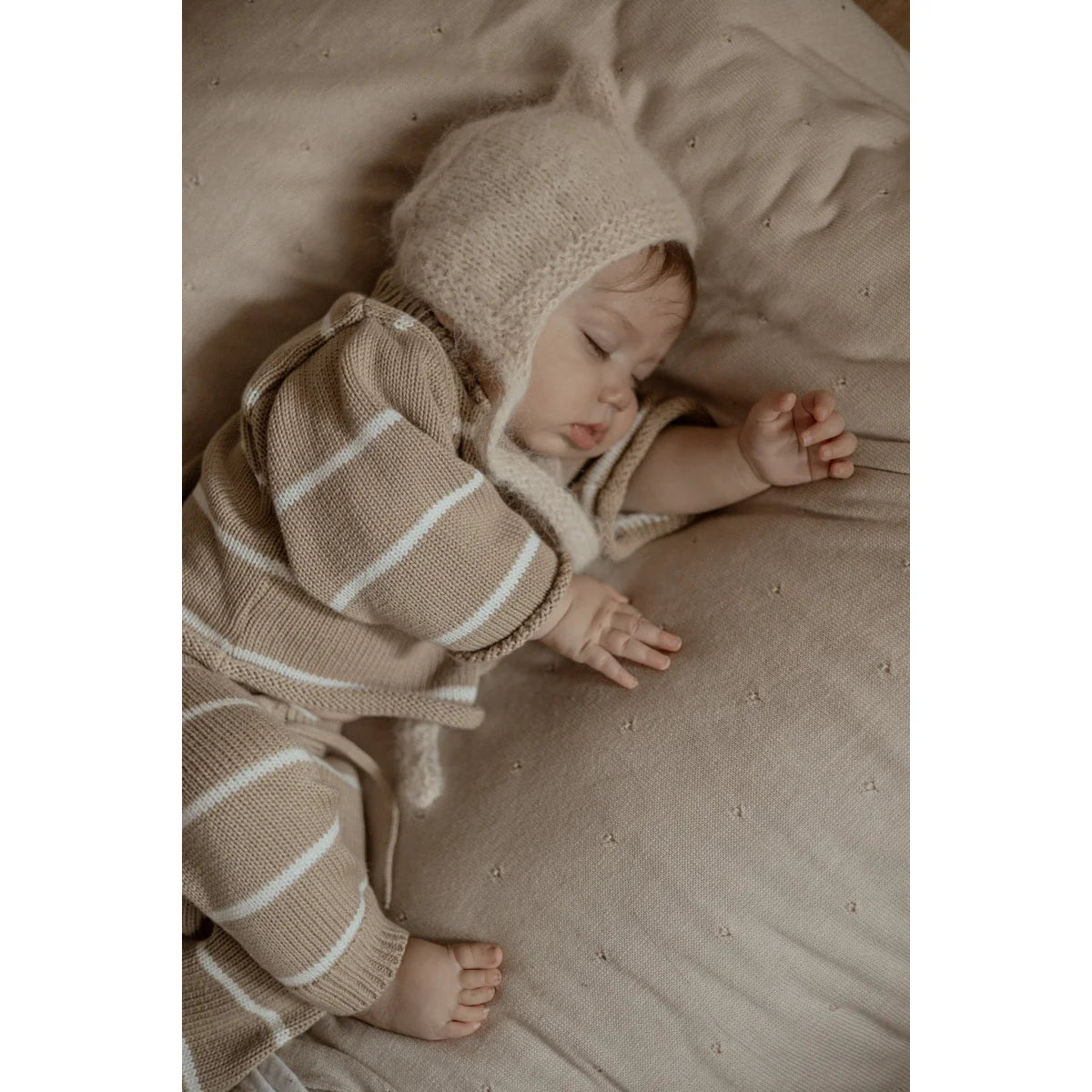 Schlafendes Baby mit weißer Mütze und gestreiftem Overall in Oversize Pullover