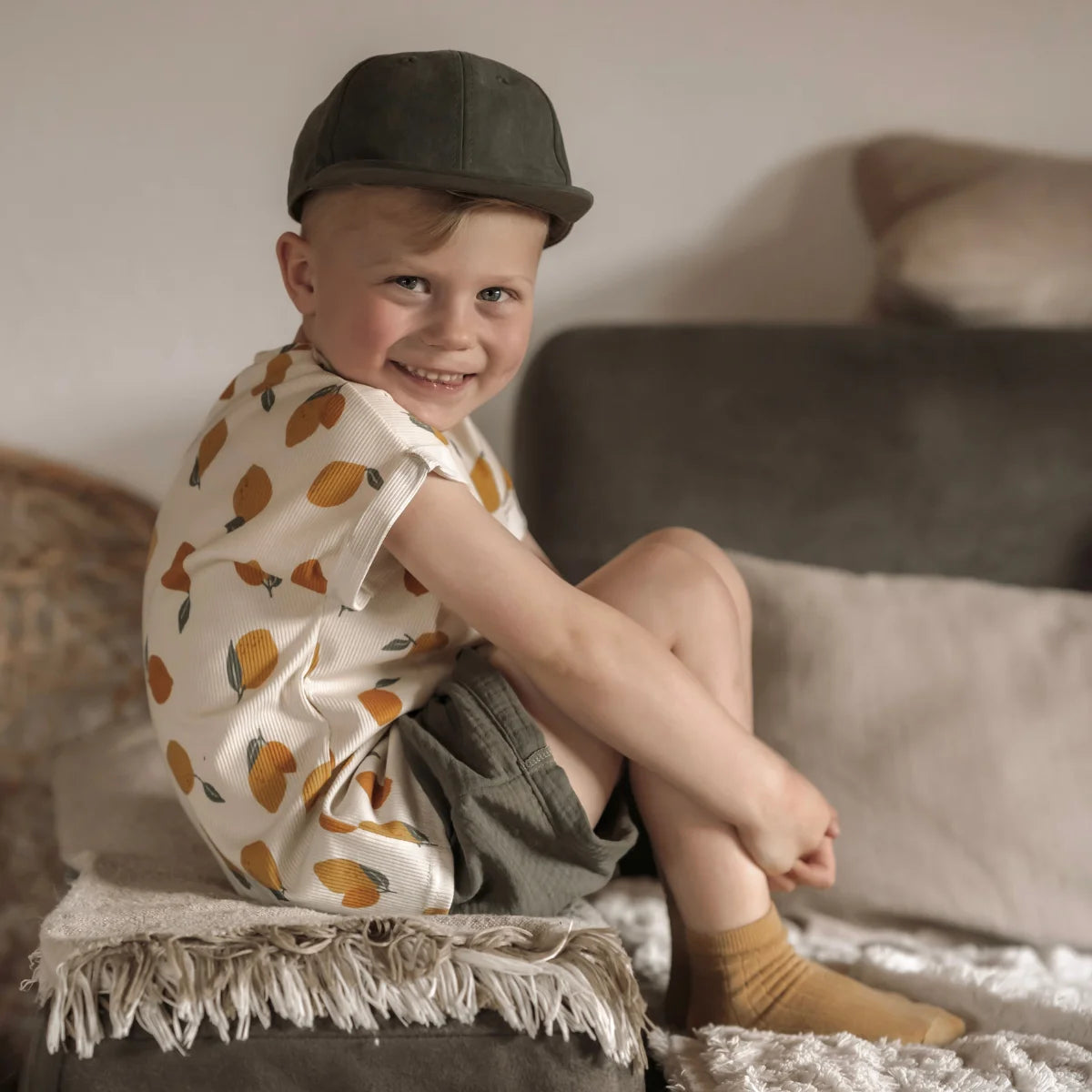 Kind trägt Oversized Shirt Rib Zitrone mit orangen Zitronen-Prints und dunkelgrüner Cap