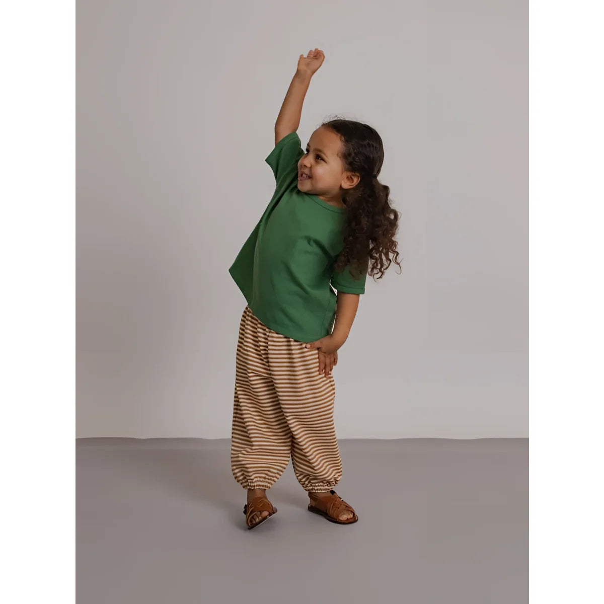 Ein kind trägt eine hose copper stripes mit kupferfarbenen streifen in beige und braun aus bequemem stoff