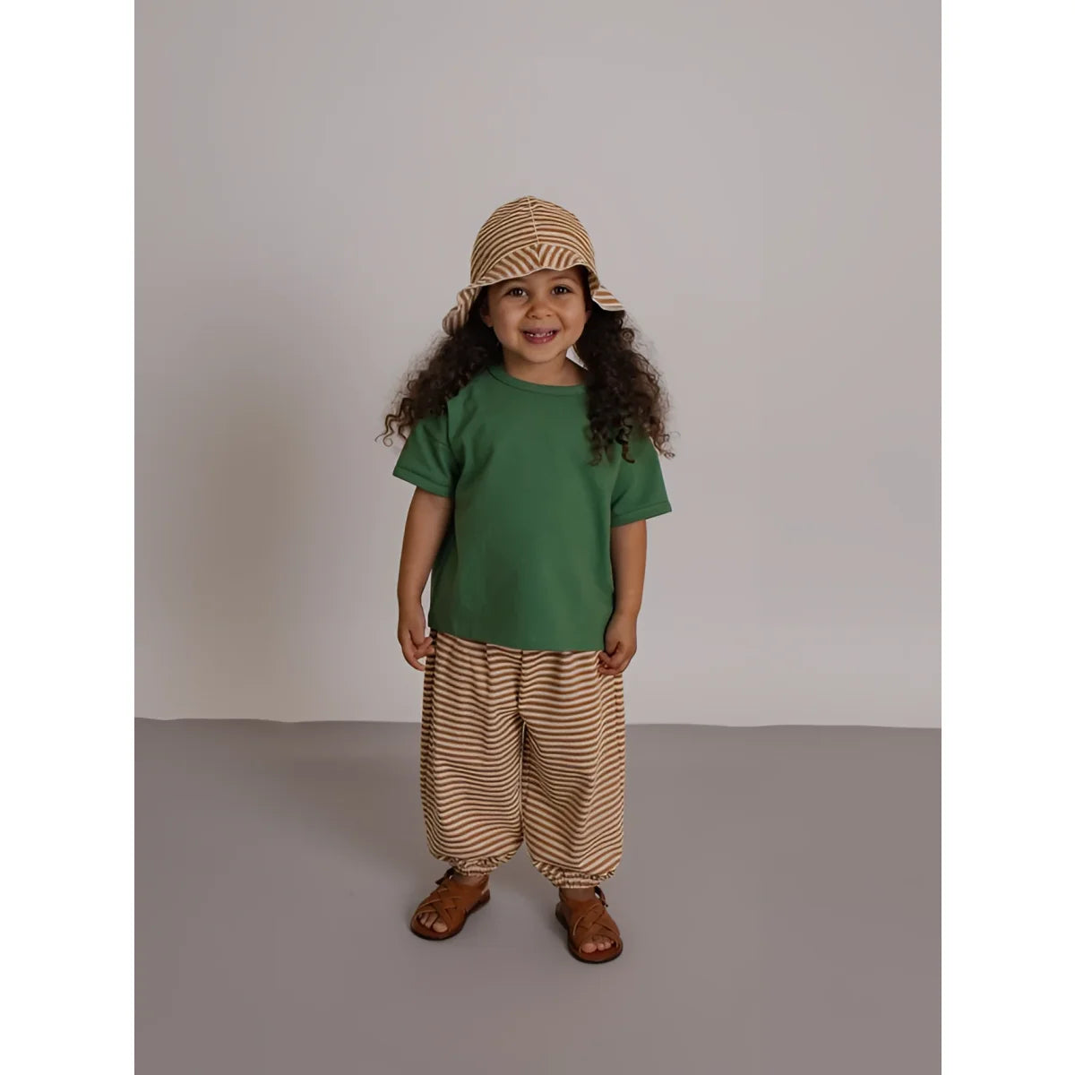 Kind trägt kupfer gestreifte weit geschnittene hose in beige und braun kombiniert mit grünem kurzarmshirt