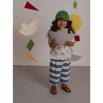 Kind trägt grüne bucket-hut und weiße und blaue gestreifte deck chair stripes hose und hält ein papierboot
