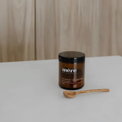Helles Amberglas mit Collagen-Drink und Holzlöffel, Postpartum Collagen Schokoladengetränk