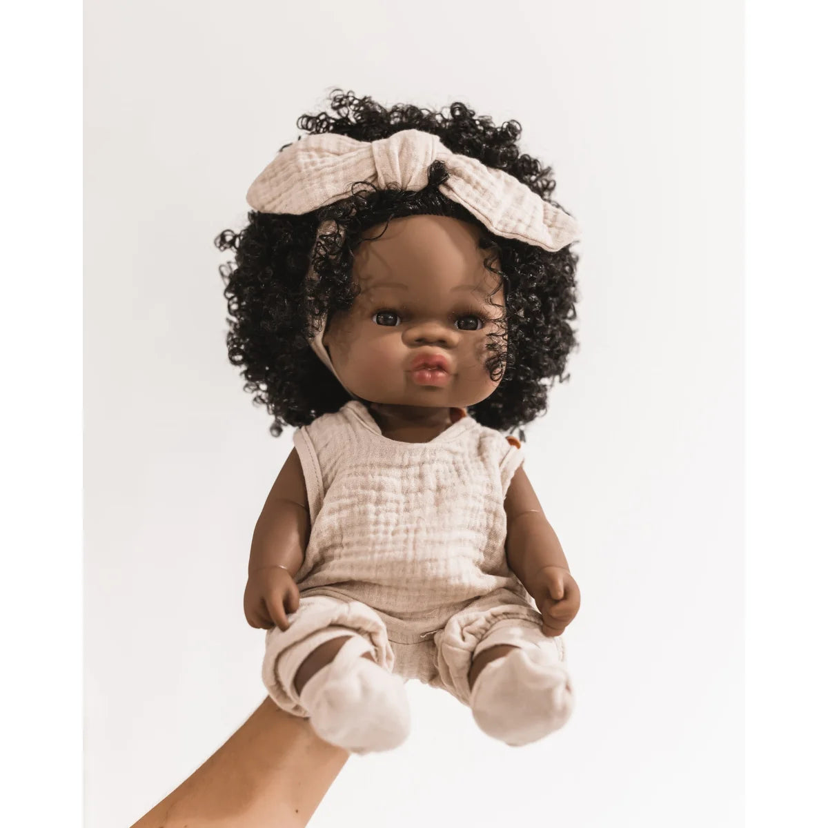 Babypuppe Loreta mit dunklem Lockenhaar in hellem Outfit und Haarschleife