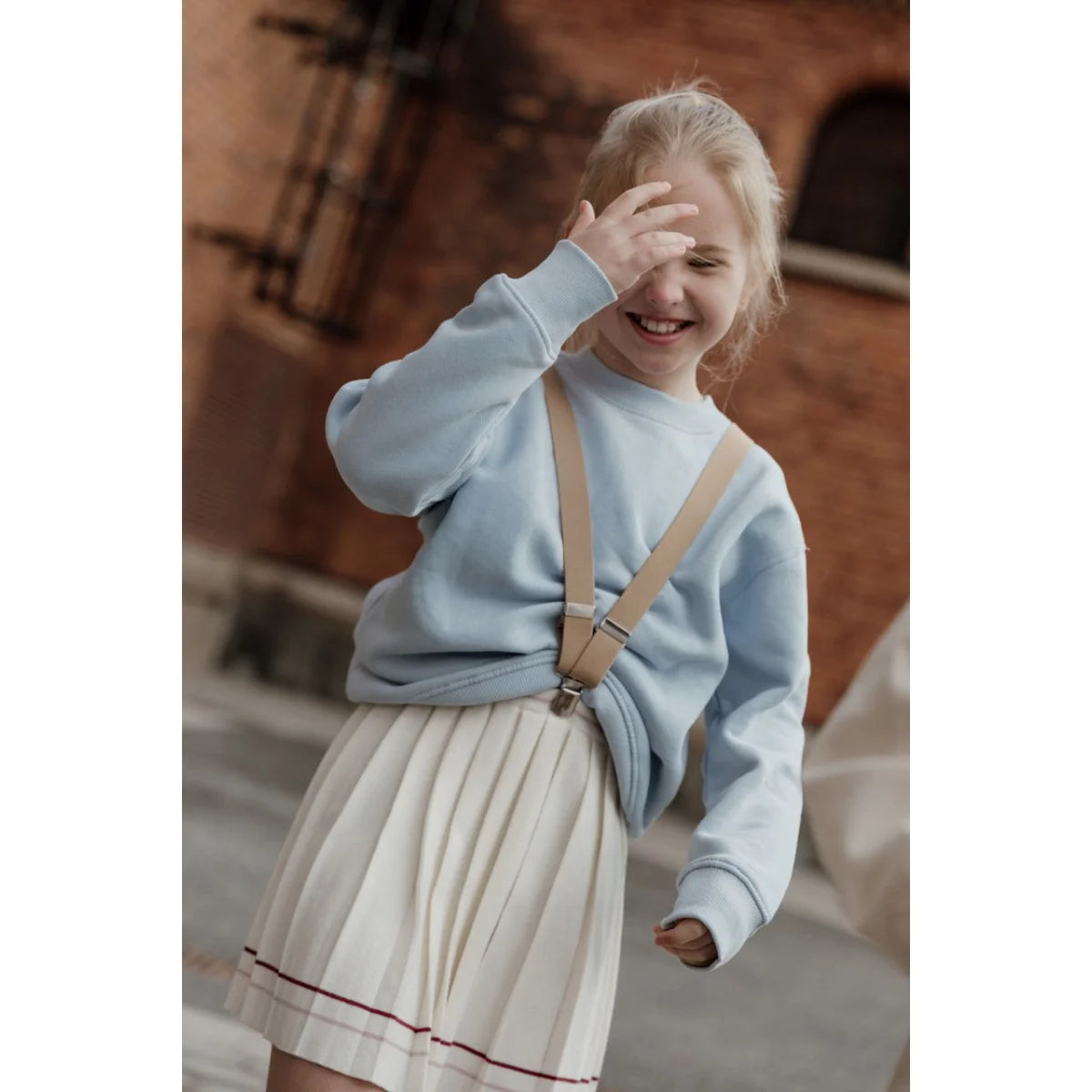 Lächelndes Mädchen in blauer Sweatshirt und plissiertem Rock mit Retro V-Trägern