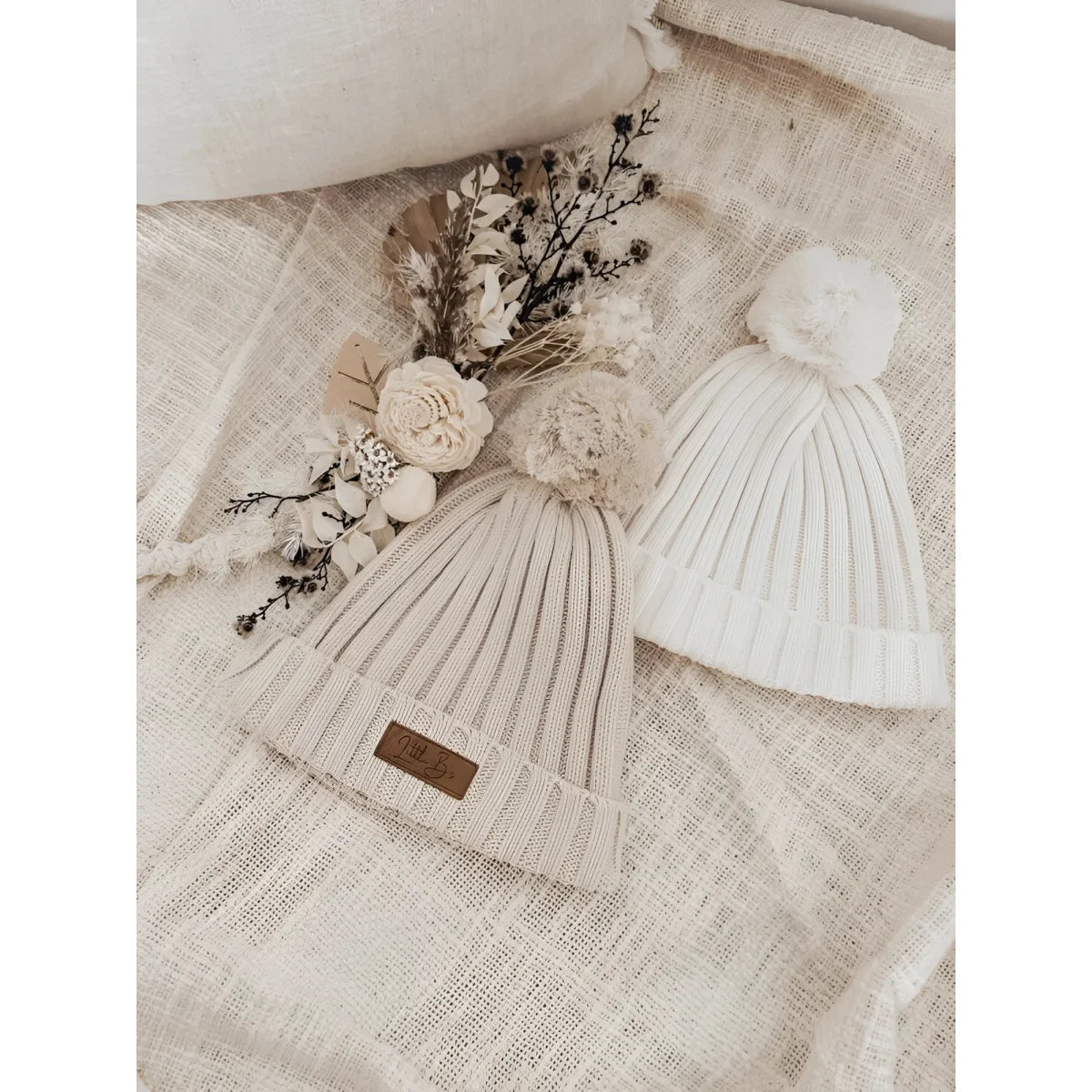 Ribbed Beanie in Milk color displayed with knitted pom-pom hats and getrockneten Blumen