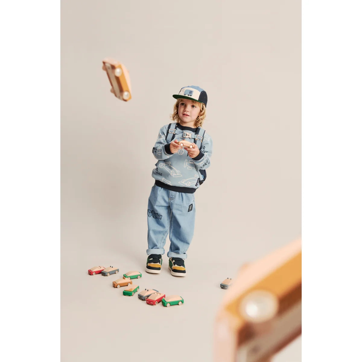 Ein kind in hellblauem sweatshirt und jeans hält holzspielzeugautos aus der rory cap cars multi mix kollektion