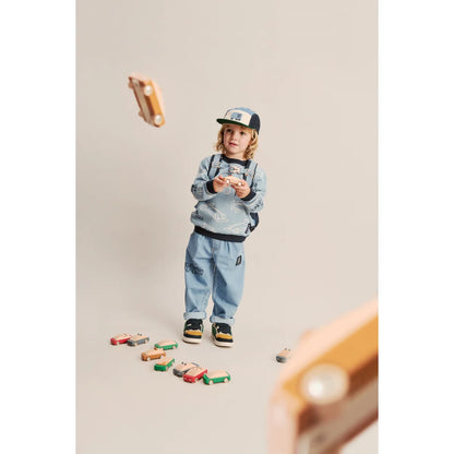 Ein kind in hellblauem sweatshirt und jeans hält holzspielzeugautos aus der rory cap cars multi mix kollektion