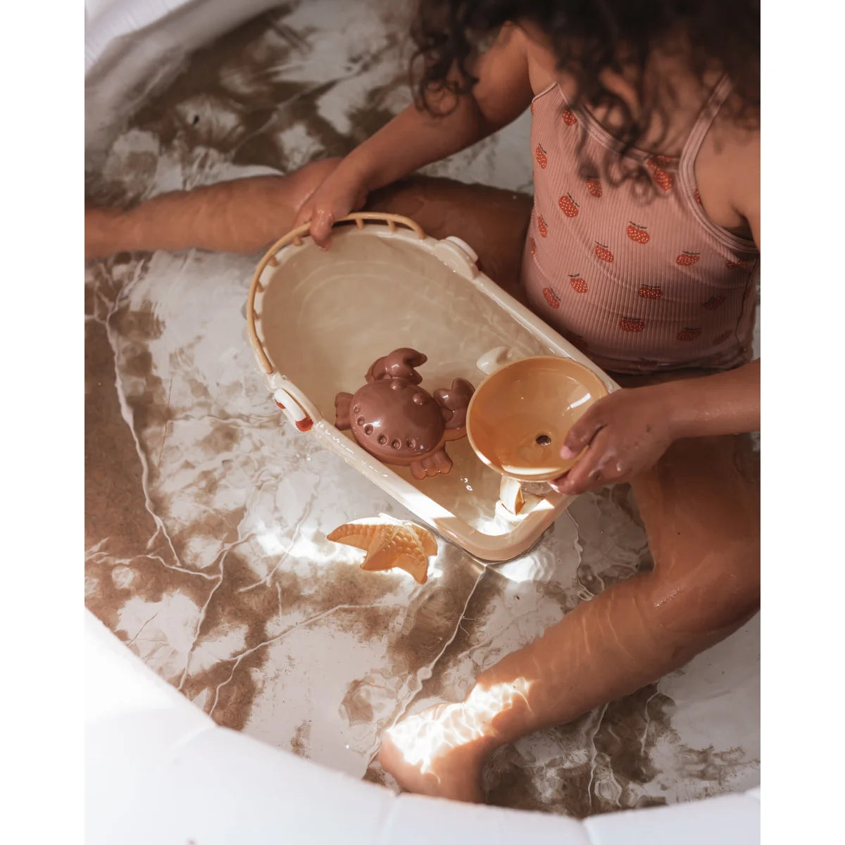 Kind spielt mit Sandspielzeug Schiff in Badewanne voller Seifenwasser