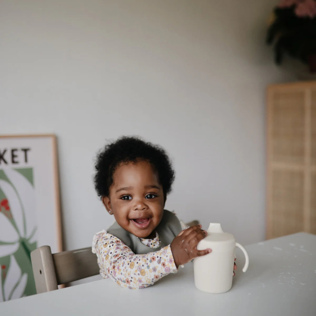 Lächelndes Kleinkind sitzt an einem Tisch mit einer weißen Tasse Schnabelbecher | Ivory