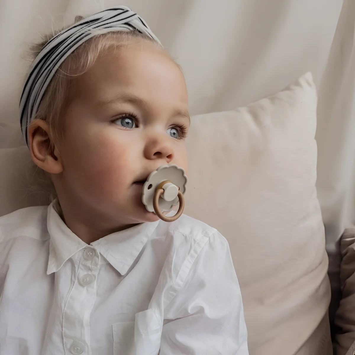 Baby mit blonden Haaren in weißem Shirt und gestreiftem Kopftuch mit Schnuller