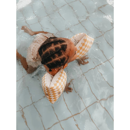 Kind schwimmt mit gelben, karierten Schwimmflügeln von Speckled Diamond