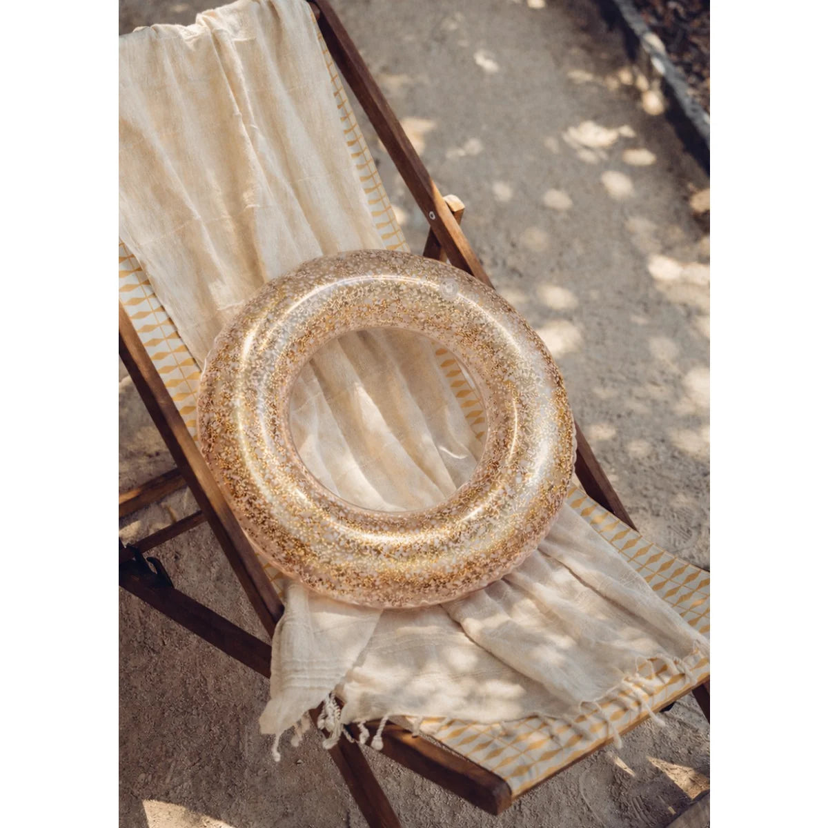 Ein transparenter goldglitzer schwimmring liegt auf einem gestreiften strandstuhl nachhaltig babykleidung schweiz