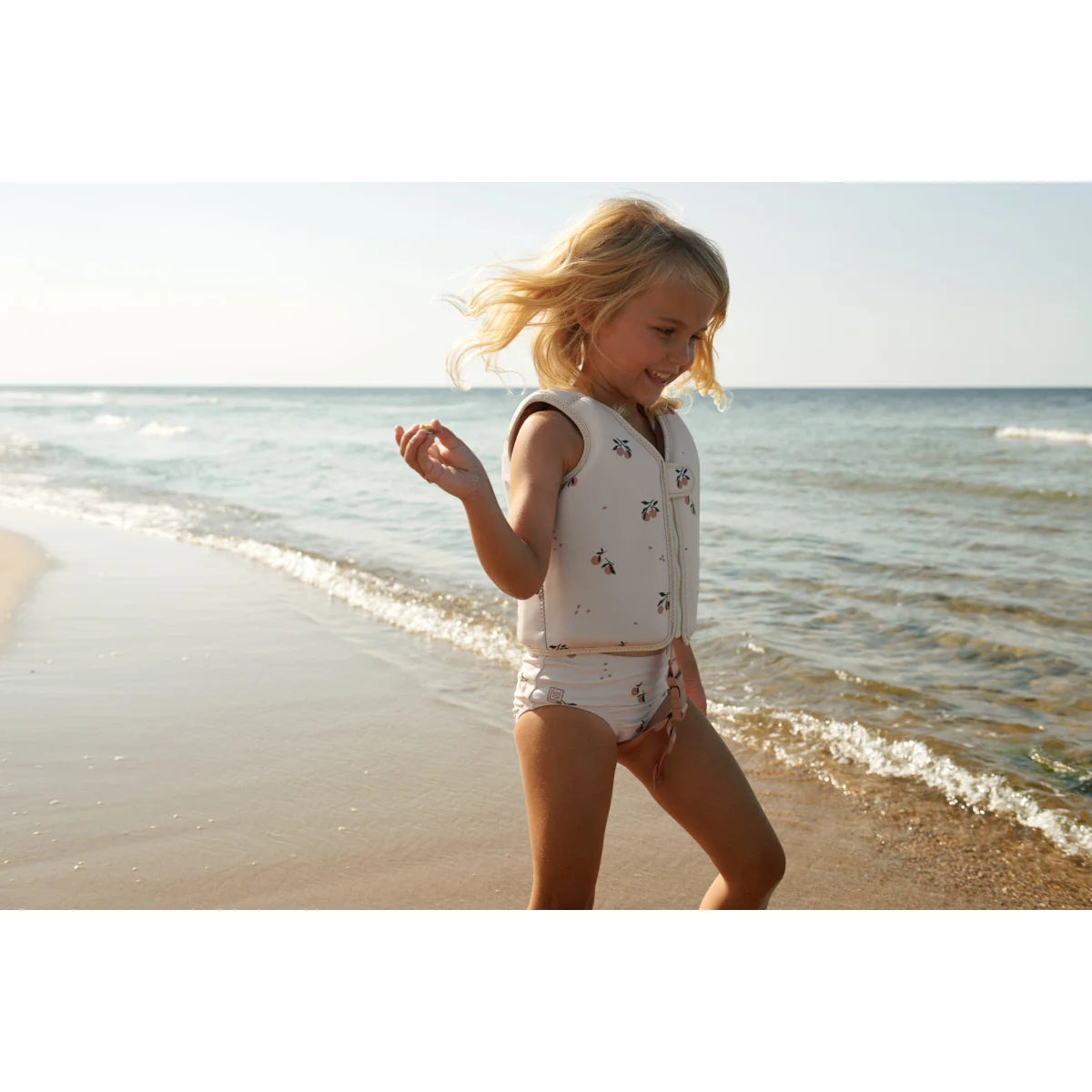 Kind spielt fröhlich am Strand mit der Schwimmweste Dove | Peach Sea shell