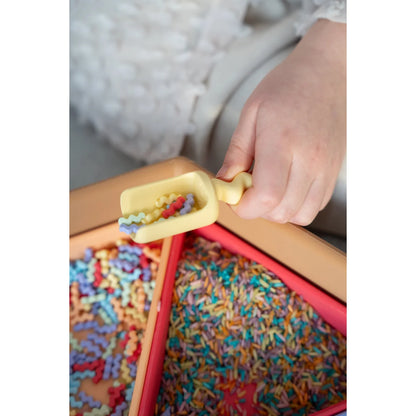Gelber plastikschöpfer gefüllt mit bunten pastastücken in sechseckiger mandigo spielschale mit dreieck-einsätzen pastel