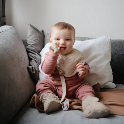 Lächelndes Baby in rosa Kleidung und Lätzchen sitzt auf einer Couch