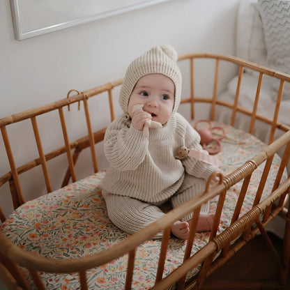 Baby im Holzbett in gestricktem Creme-Outfit und Mütze neben Silikon Lamm Beisstier