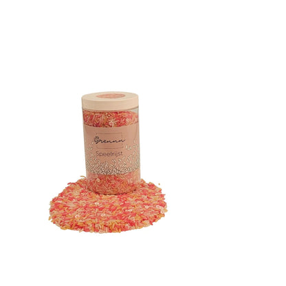 Ein klarer zylinderbehälter mit beigem deckel und etikett gefüllt mit pinken und orangen streuseln spielreis-mischung pink